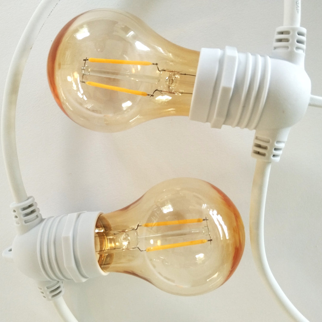 Two clear glass LED filament light bulbs with white screw bases and white cords, shown against a plain light background.