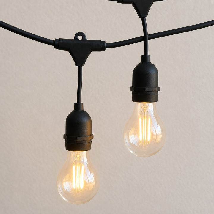 Black outdoor string light fixture with two hanging clear Edison-style bulbs illuminated against a plain light beige wall.